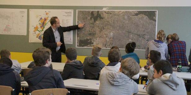 Ein Lehrer erklärt einer Klasse eine Karte an der Wand.