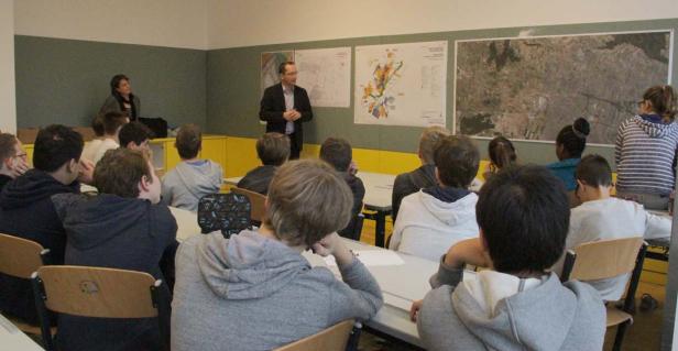 Ein Lehrer hält einen Vortrag vor einer Klasse mit Karten an der Wand.