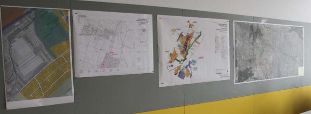 An einer Wand hängen vier verschiedene Karten und Pläne.