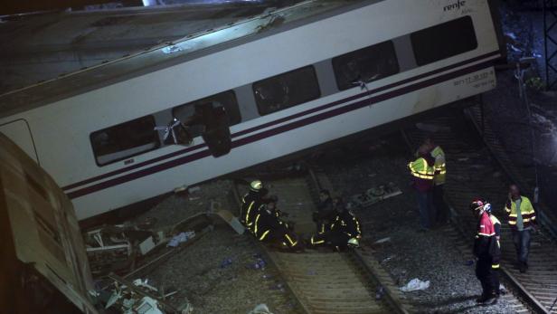 Ein verunglückter Renfe-Zug liegt neben den Gleisen, umgeben von Rettungskräften.