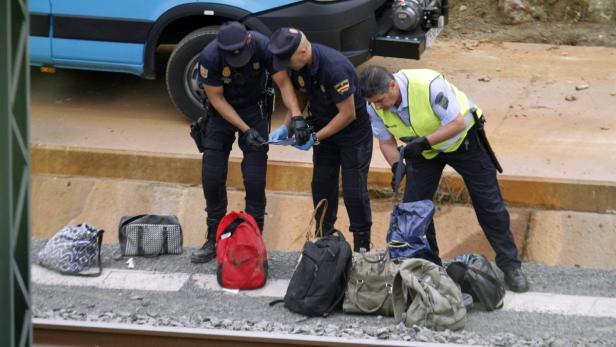 Drei Polizisten untersuchen Gepäckstücke auf einem Bahngleis.