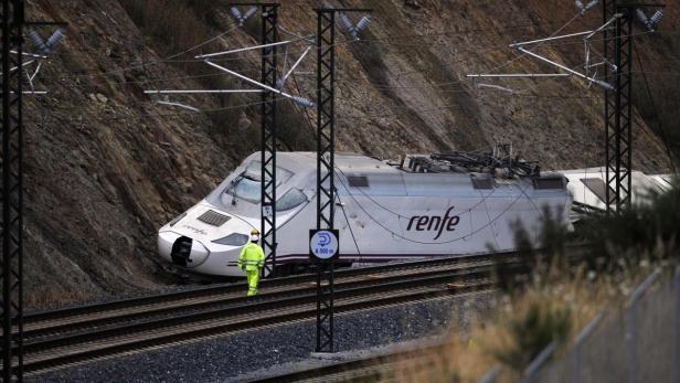 Ein beschädigter RENFE-Hochgeschwindigkeitszug steht neben einem Gleis, während ein Arbeiter in Sicherheitskleidung vorbeigeht.