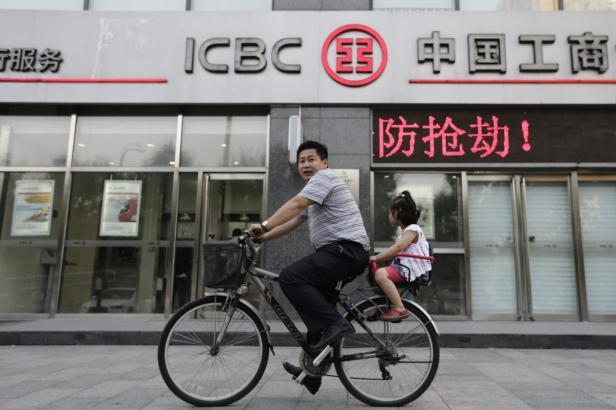 Ein Mann fährt mit einem Kind auf dem Fahrrad vor einer Filiale der ICBC-Bank.