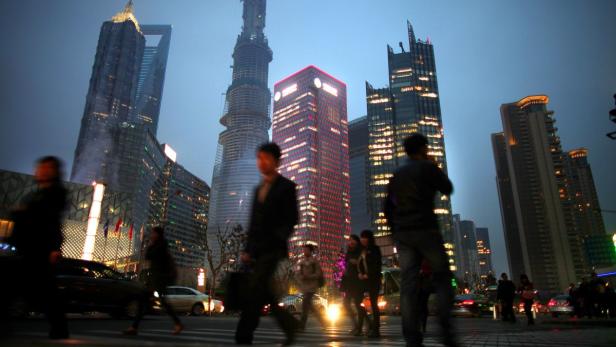 Menschen überqueren eine Straße in Shanghai bei Nacht, Wolkenkratzer im Hintergrund.