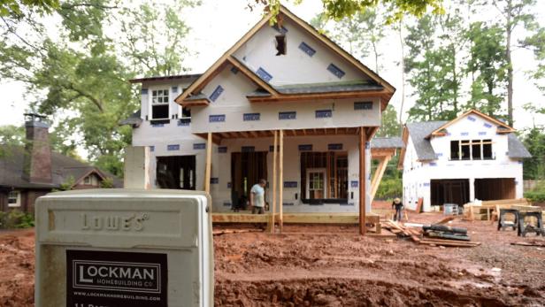 Im Bau befindliche Häuser mit freiliegendem Holzrahmen und Bauarbeitern auf einem Grundstück.