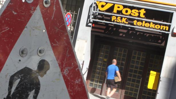 Ein Mann betritt ein Postamt, im Vordergrund ein Warnschild für Bauarbeiten.