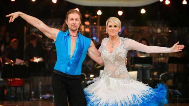 Ein Mann und eine Frau tanzen in glitzernden Kostümen auf einer Bühne.