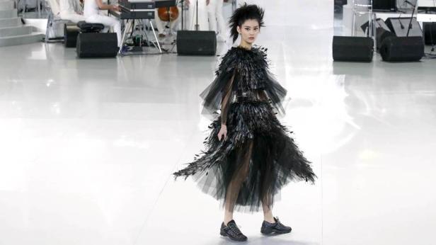 Ein Model präsentiert ein schwarzes Federkleid auf einem Laufsteg.