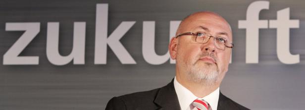 Ein Mann mit Brille und Anzug steht vor dem Schriftzug „Zukunft“.