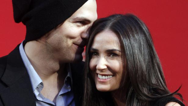 Ashton Kutcher flüstert Demi Moore auf einem roten Teppich etwas ins Ohr.