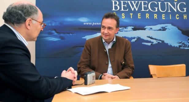 Zwei Männer sitzen an einem Tisch vor einem Banner der „Bewegung Österreich“.