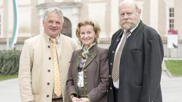 Drei Personen in Tracht posieren vor einem Gebäude.