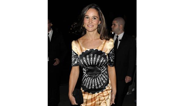 Pippa Middleton lächelt in einem gemusterten Kleid und mit einer Clutch in der Hand.