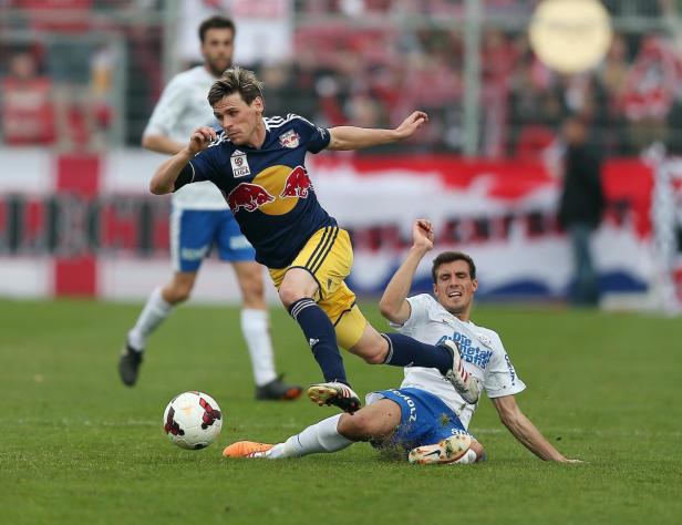 Ein Fußballspieler von Red Bull Salzburg grätscht einen Gegenspieler ab.