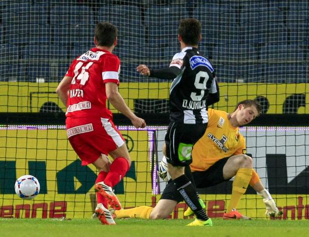 Ein Fußballspiel mit Spielern in roten, schwarzen und gelben Trikots vor einem Tornetz.