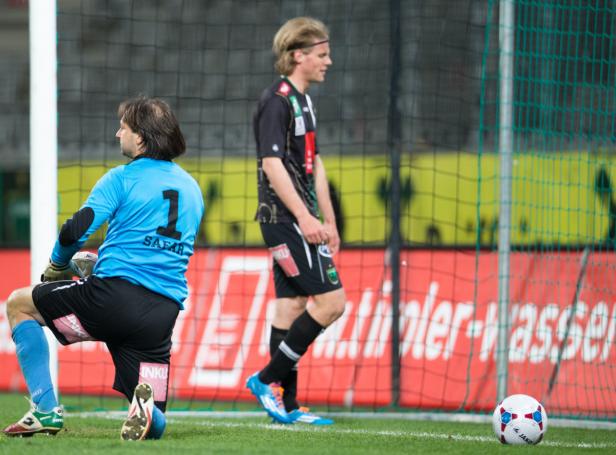 Ein Fußballtorwart kniet neben einem Fußballspieler auf dem Spielfeld.