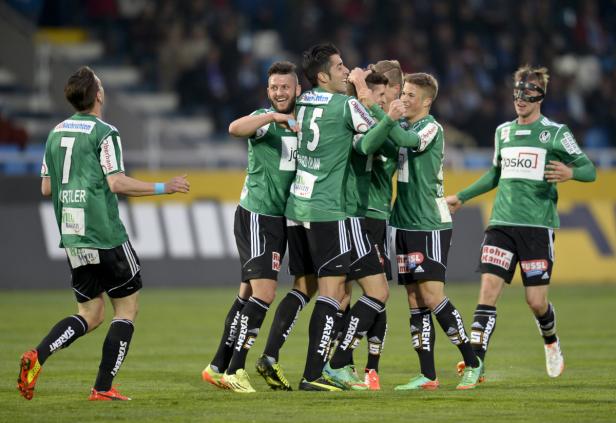 Eine Gruppe Fußballspieler in grünen Trikots umarmt sich auf dem Spielfeld.