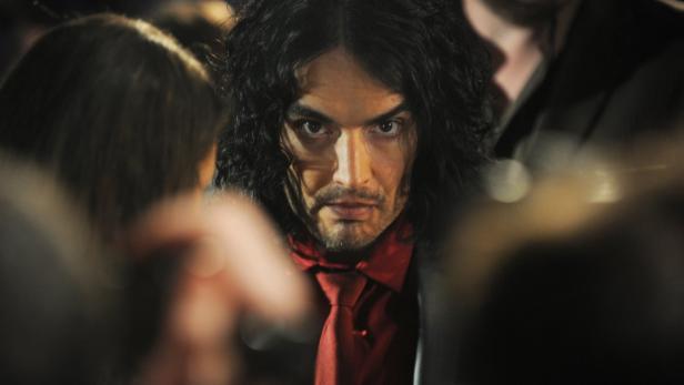 Ein Mann mit langen, dunklen Haaren und roter Krawatte blickt ernst in die Kamera.