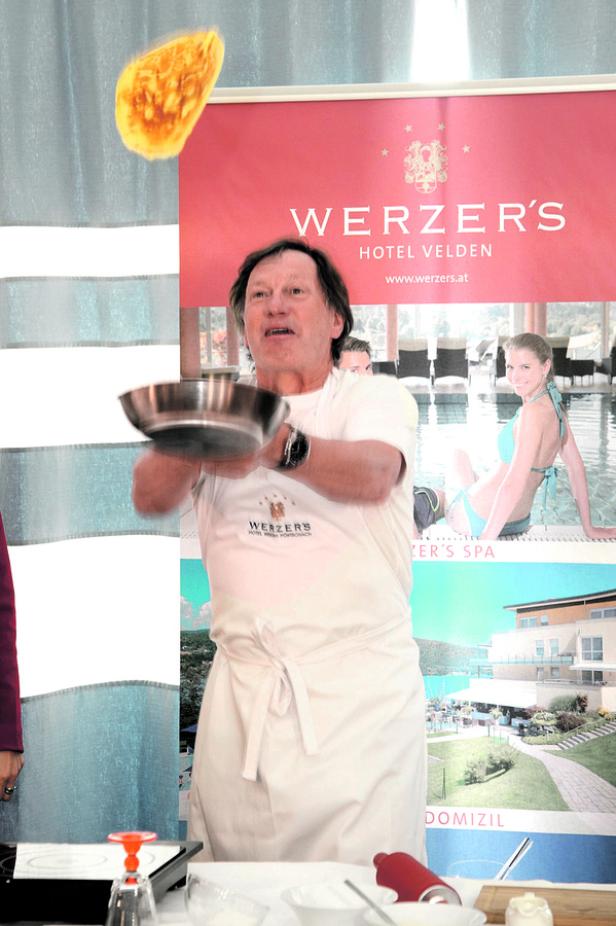 Ein Koch wirft einen Pfannkuchen in die Luft vor einem Werbebanner des Werzer's Hotel Velden.