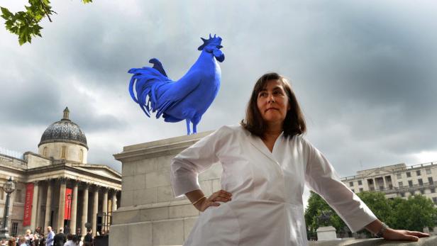 Eine Frau posiert vor dem Trafalgar Square mit einem großen blauen Hahn im Hintergrund.