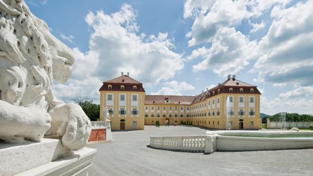 Das Schloss Hof mit einem Löwendenkmal und einem Brunnen im Vordergrund.