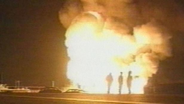 Drei Personen stehen vor einer großen Feuerwolke in der Nacht.
