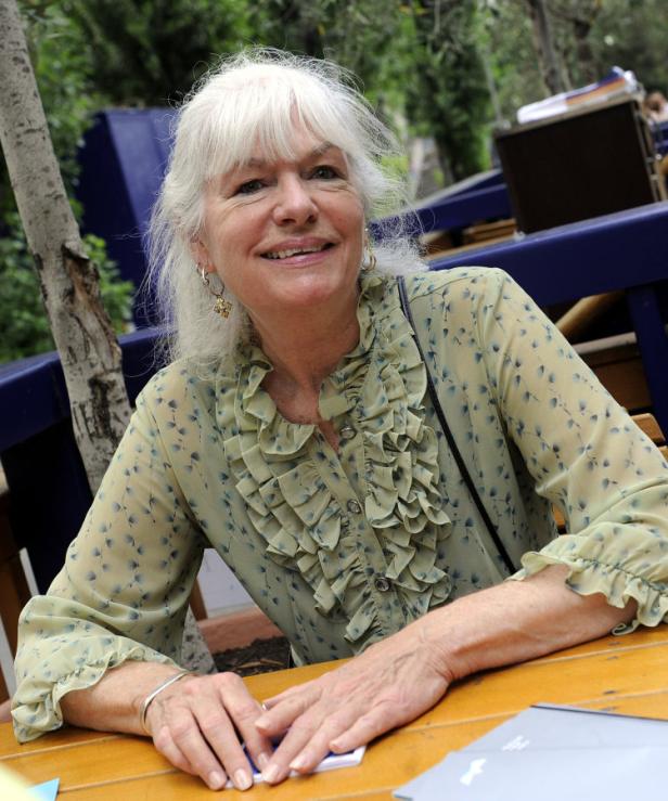 Eine ältere Frau mit weißem Haar sitzt an einem Tisch im Freien.