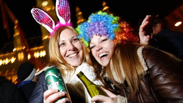 Zwei Frauen feiern mit Getränken und bunten Kostümen im Freien.