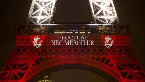 Der Eiffelturm in roter Beleuchtung mit dem Pariser Wappen und dem Motto „Fluctuat nec mergitur“.