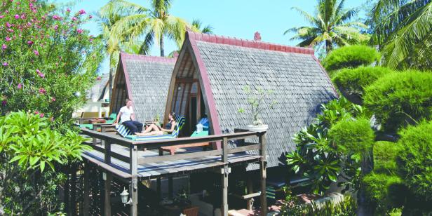 Zwei Personen entspannen auf der Terrasse eines Bungalows in einer tropischen Umgebung.