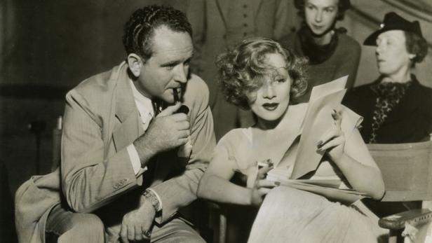Marlene Dietrich und ein Mann mit Pfeife sitzen zusammen und lesen Drehbücher.