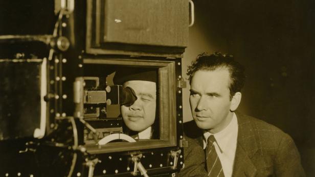 Ein Mann blickt durch eine Kamera, während ein anderer Mann daneben steht.