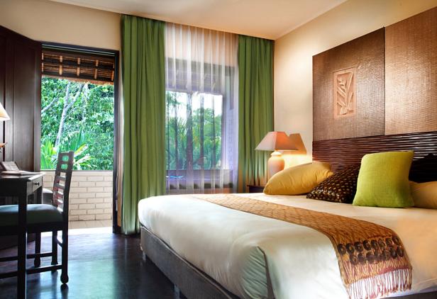 Ein helles Hotelzimmer mit einem Bett und Blick auf üppiges Grün.