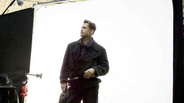 Brad Pitt in einem dunklen Mantel steht vor einem hellen Hintergrund.