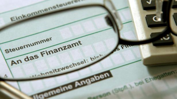 Ein Steuerformular mit der Aufschrift „An das Finanzamt“ liegt unter einer Brille und einem Taschenrechner.