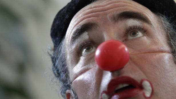 Das Gesicht eines Clowns mit roter Nase und weißer Schminke blickt nach oben.