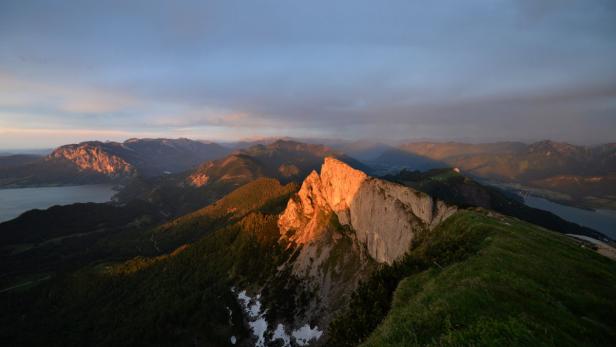 Blick von einem Berggipfel auf eine Berglandschaft im Abendlicht.