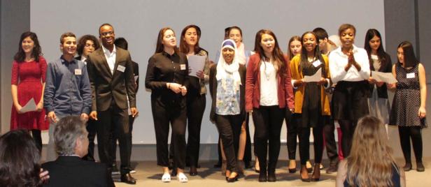 Eine diverse Gruppe junger Menschen steht auf einer Bühne und singt.