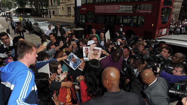 Eine Menschenmenge umringt eine Person, die Autogramme gibt, während Fotografen Fotos machen.