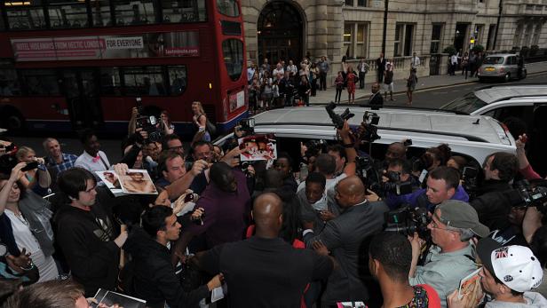 Eine Menschenmenge mit Fotografen drängt sich vor einem Gebäude und einem roten Doppeldeckerbus.