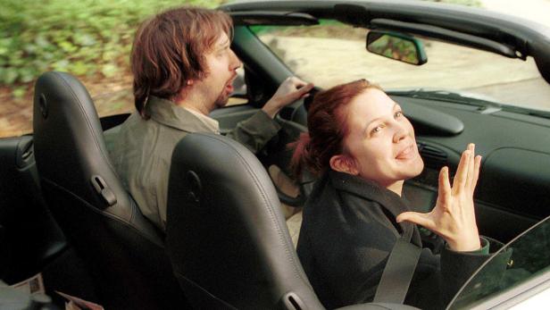 Drew Barrymore und ein Mann fahren in einem offenen Sportwagen.