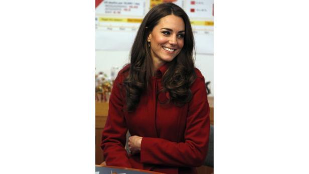 Catherine, Princess of Wales, lächelt in einem roten Mantel.