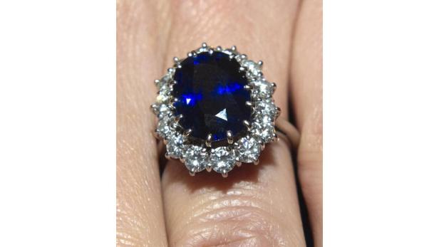 Ein Finger trägt einen Ring mit einem großen blauen Saphir, umgeben von Diamanten.