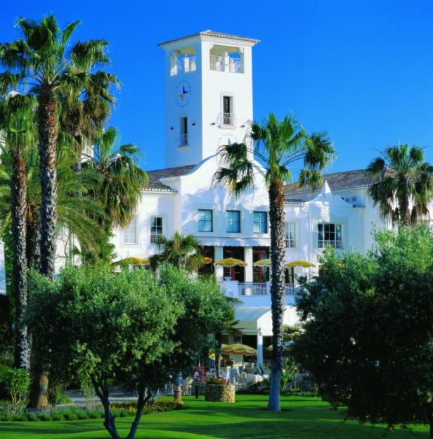 Ein weißes Gebäude mit einem Turm und Palmen unter blauem Himmel.