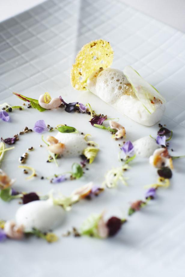 Ein kunstvoll angerichtetes Gericht mit Meeresfrüchten, Blüten und Schäumen auf einem weißen Teller.