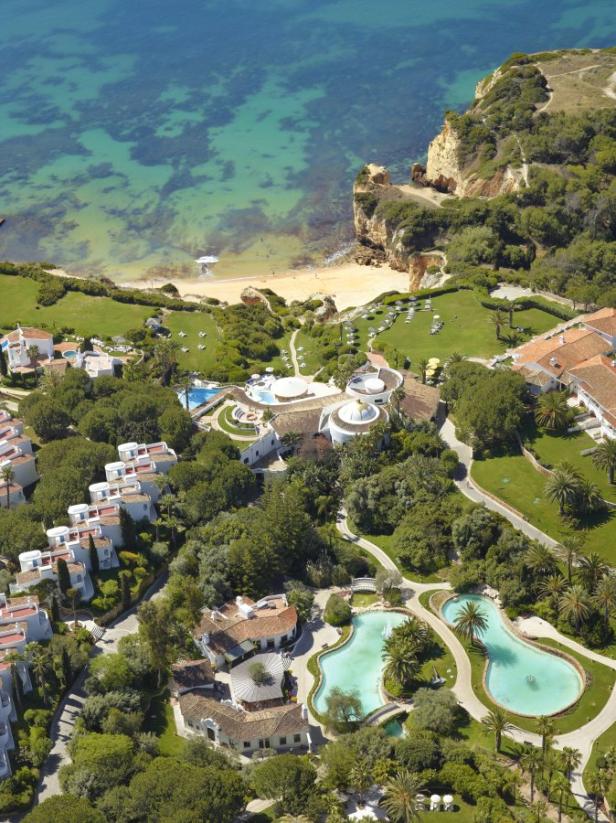 Luftaufnahme eines Resorts mit Pools, Gärten und einem Strand an der Küste.