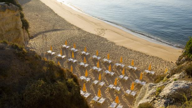 Blick von oben auf einen Strand mit Liegestühlen und Sonnenschirmen.