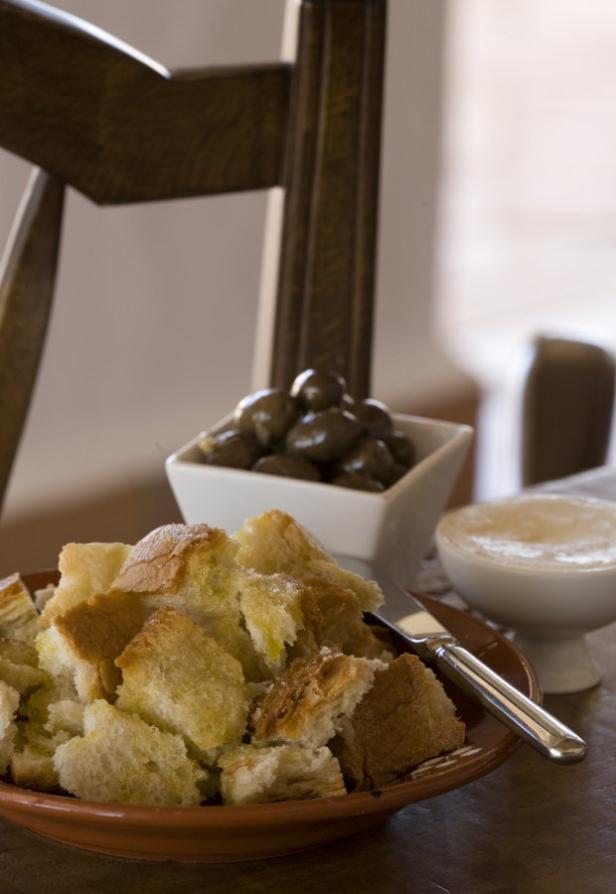 Ein Teller mit Brotwürfeln, eine Schale Oliven und ein Dip stehen auf einem Tisch.