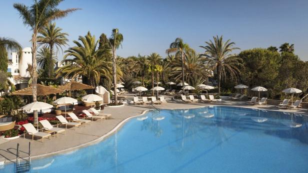 Ein großer Swimmingpool mit Liegestühlen und Palmen in einem Resort.