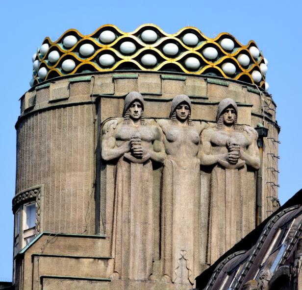 Drei Statuen von muskulösen Frauen zieren ein Gebäude mit einer goldenen Krone.